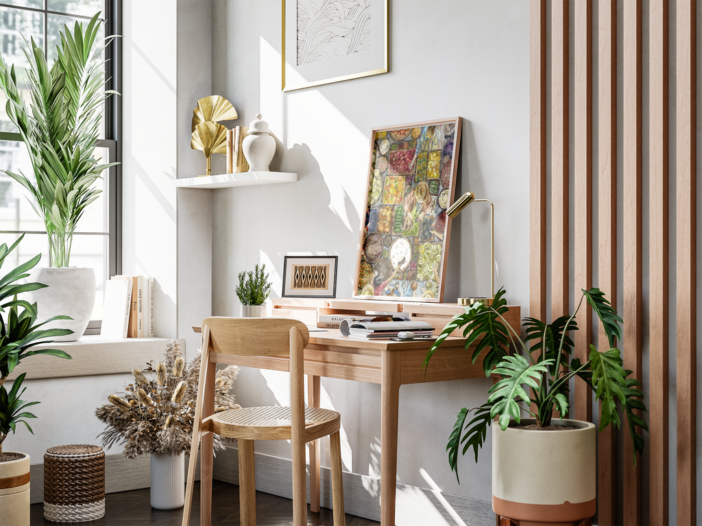 A styled interior corner with a light wood desk and matching chair against a white wall, decorated with framed art, a shelf, books, dried flowers, and several green houseplants in ceramic pots.
