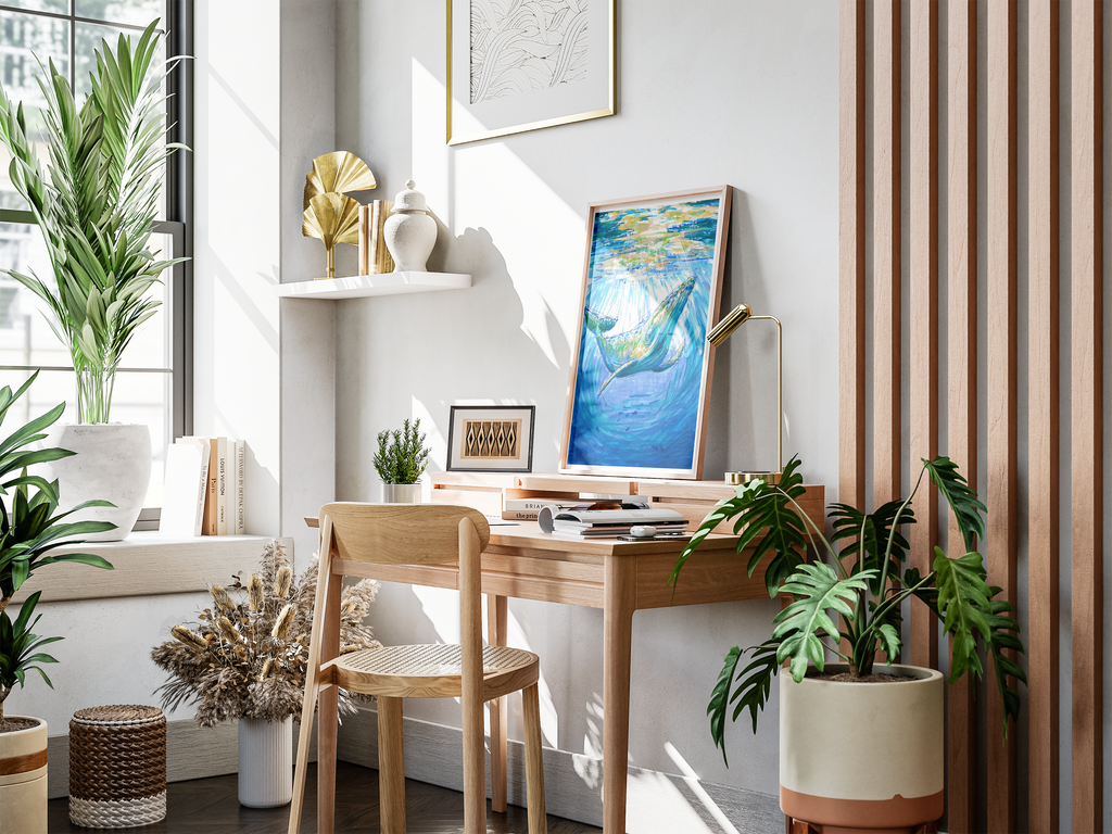 A styled interior corner with a wooden desk and chair, potted plants, a shelf with decorative objects, and a framed blue whale artwork leaning against the wall.